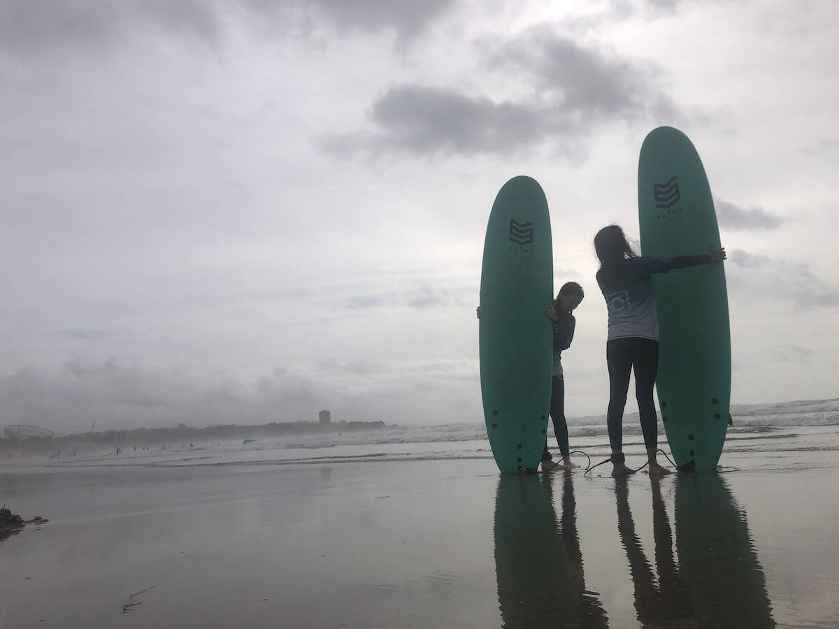 Two surfers stand on a beach