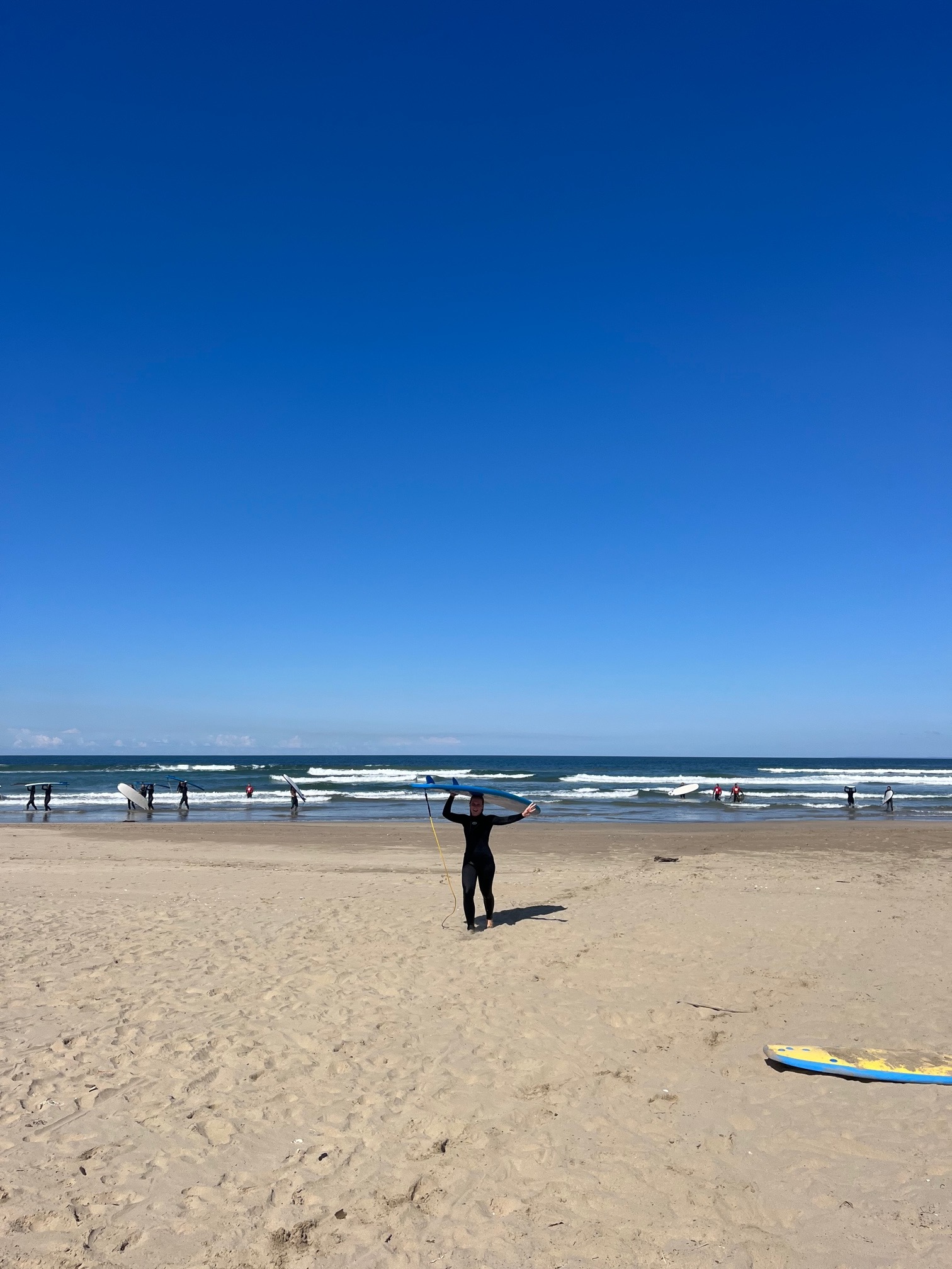 Morgan Limbaugh on the beach carrying a surfboard over her head.