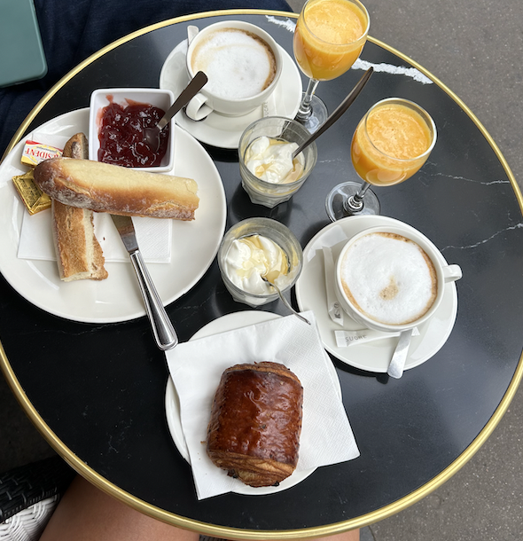 Various foods on a table including danishes and breads, cream, jam, orange juice, and coffee