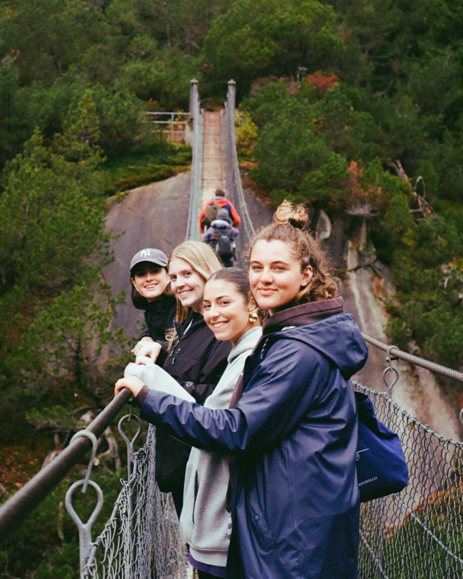 student with group of friends walking across a suspended bridge