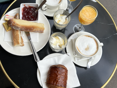 Various foods on a table including danishes and breads, cream, jam, orange juice, and coffee