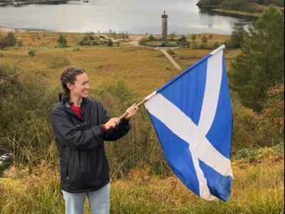 student holding Scotland's national flag with the Glenfinnan Monument on the background
