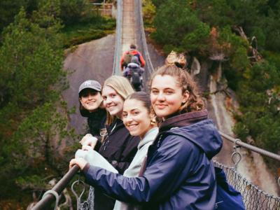 student with group of friends walking across a suspended bridge