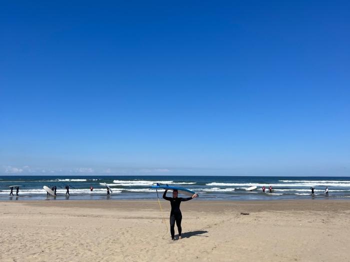 Morgan Limbaugh on the beach carrying a surfboard over her head.