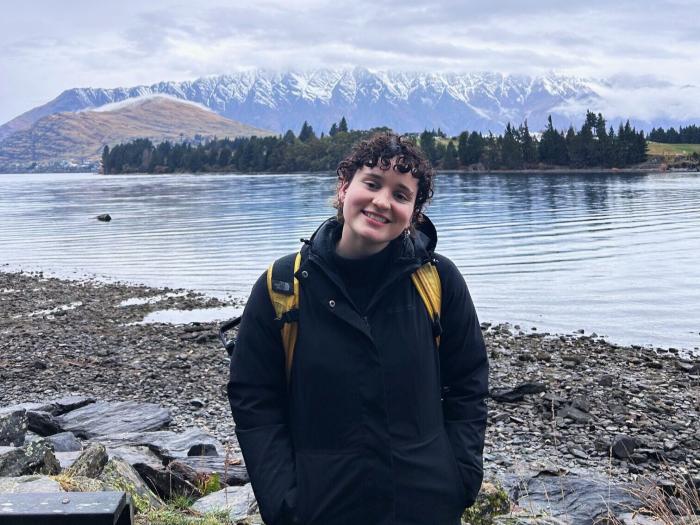 student posing in front of a lake with snow covered mountains in the background