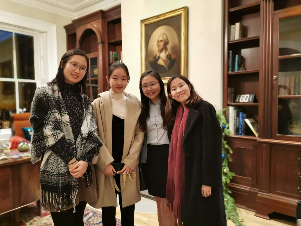 Four GW exchange students posing for a photo in front of a portrait of George Washington in the University President's office.