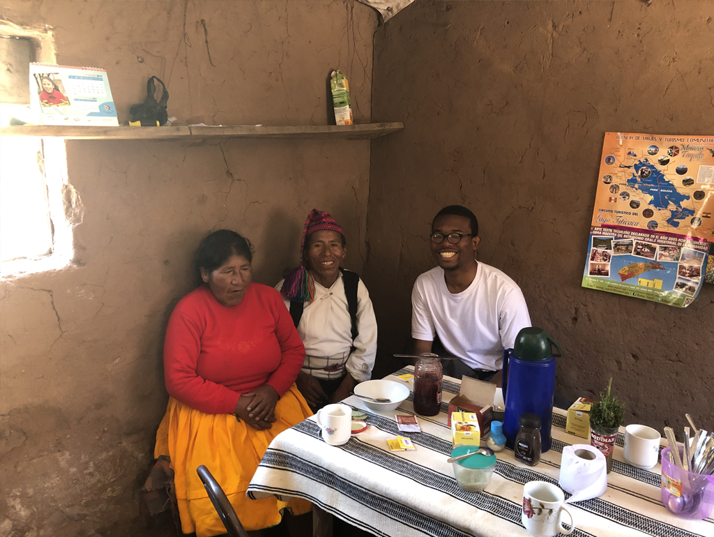 GBP student Ojani Walthrust smiles for a photograph while sitting at a table with a man and woman in Peru.